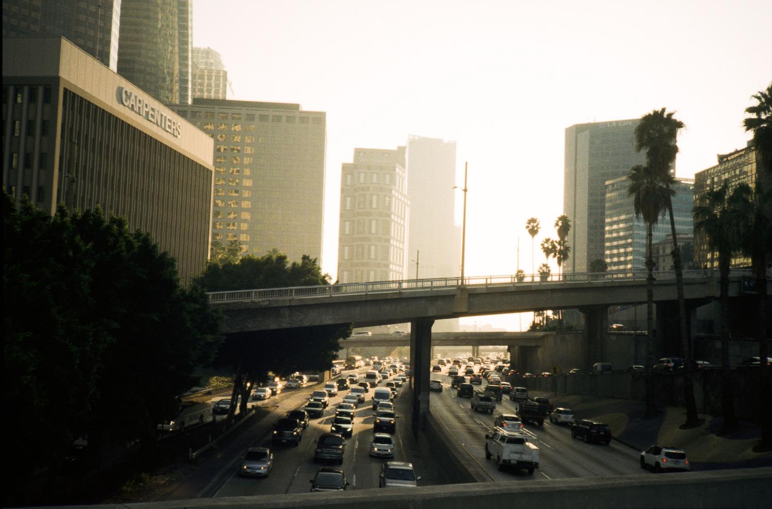 Tráfico denso en una autopista de Los Ángeles con rascacielos al fondo, ilustrando la densidad del mundo abierto.