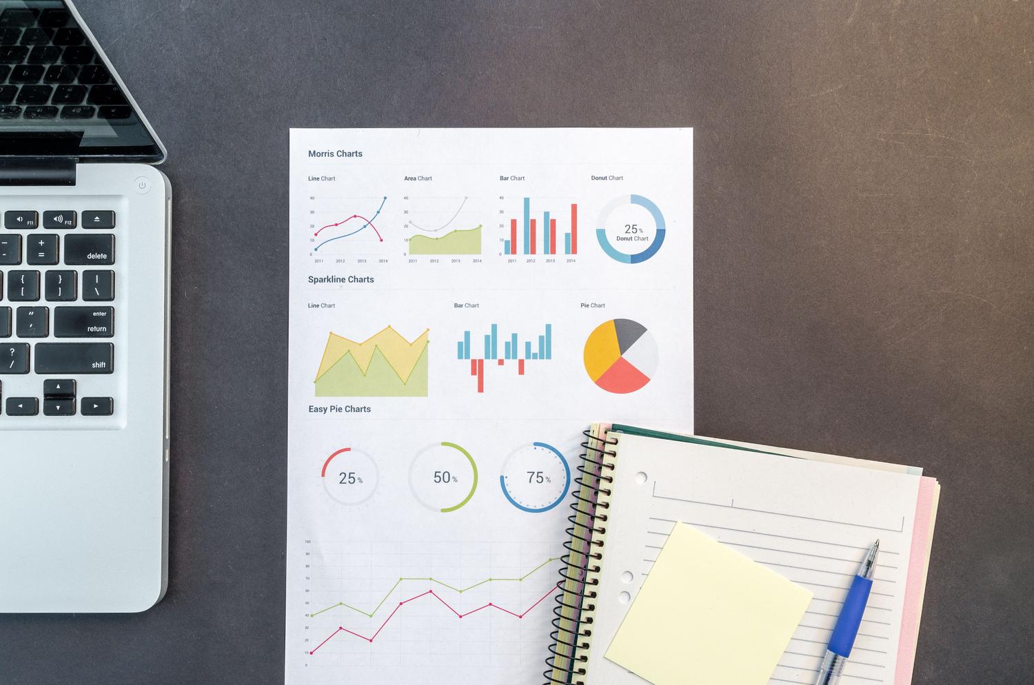 Escritorio con gráficos de datos y un ordenador portátil, ilustrando la organización de la información.