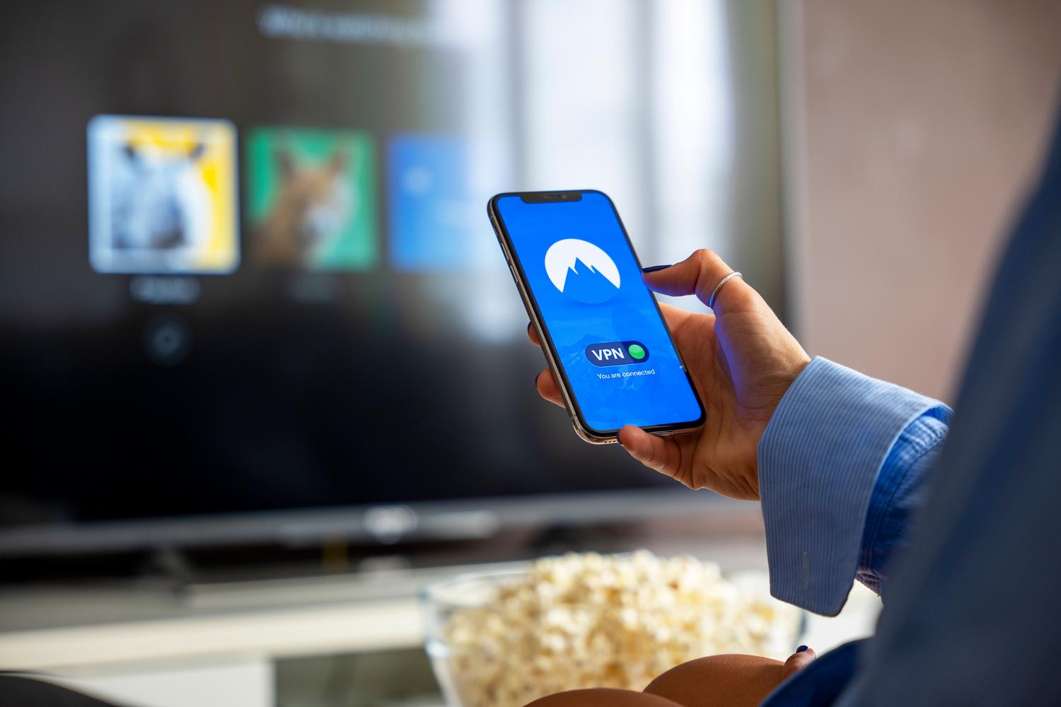 Persona utilizando una VPN en su iPhone mientras ve contenido en una Smart TV, ilustrando la capacidad de saltar bloqueos geográficos.