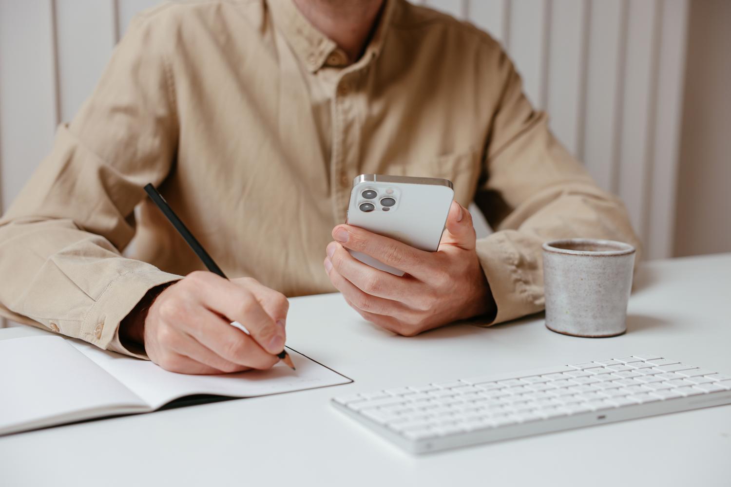 Persona organizando tareas en un cuaderno mientras consulta su smartphone, ilustrando la multitarea en la gestión de cuentas.