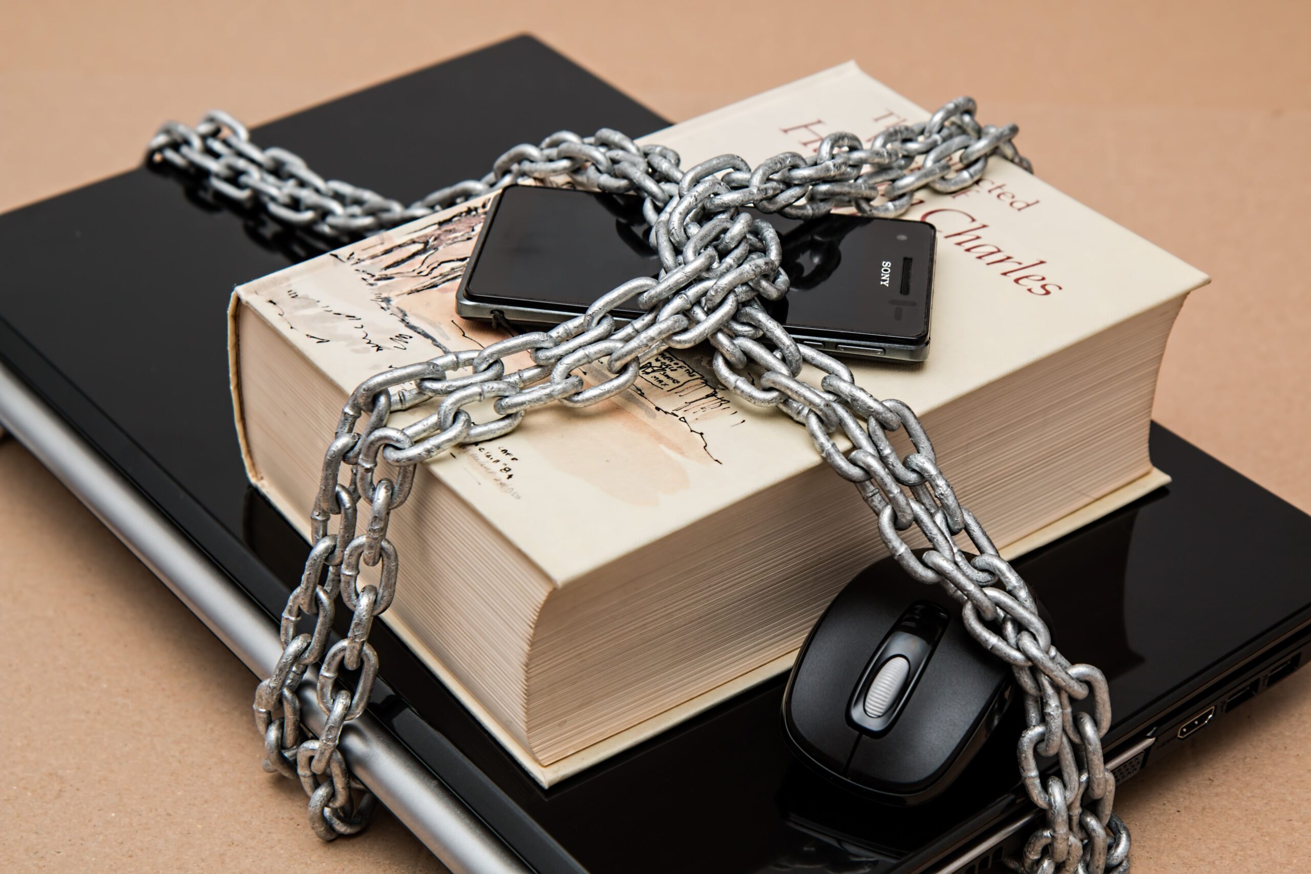 Laptop, móvil y libro encadenados simbolizando la protección y el blindaje de los accesos digitales.