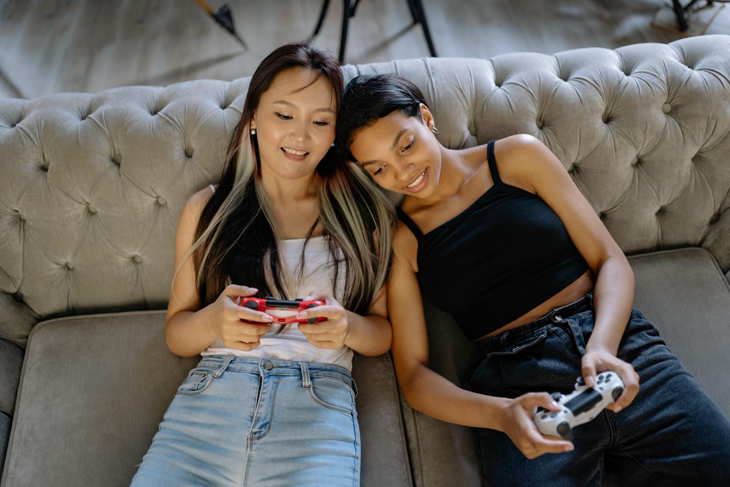 Dos mujeres relajadas jugando a videojuegos juntas en un cómodo sofá.