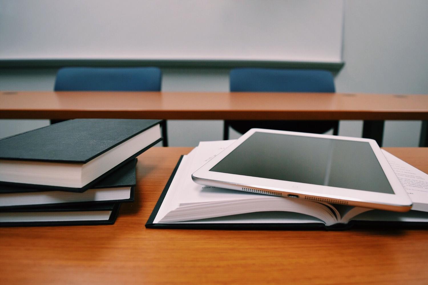 Tablet y libros de texto sobre una mesa, representando la creación de cuestionarios educativos.