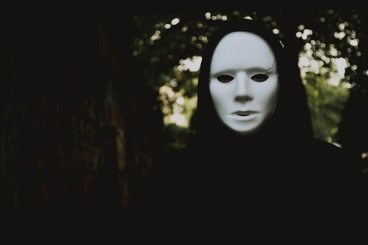 Figura misteriosa con una máscara blanca en un bosque oscuro y brumoso, representando la atmósfera inquietante y los entes típicos de los creepypastas.