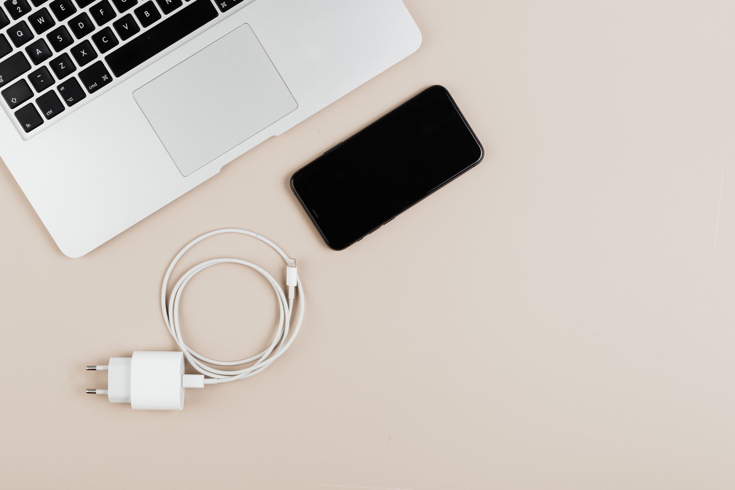 Composición cenital de un ordenador portátil, smartphone y cargador sobre un fondo neutro