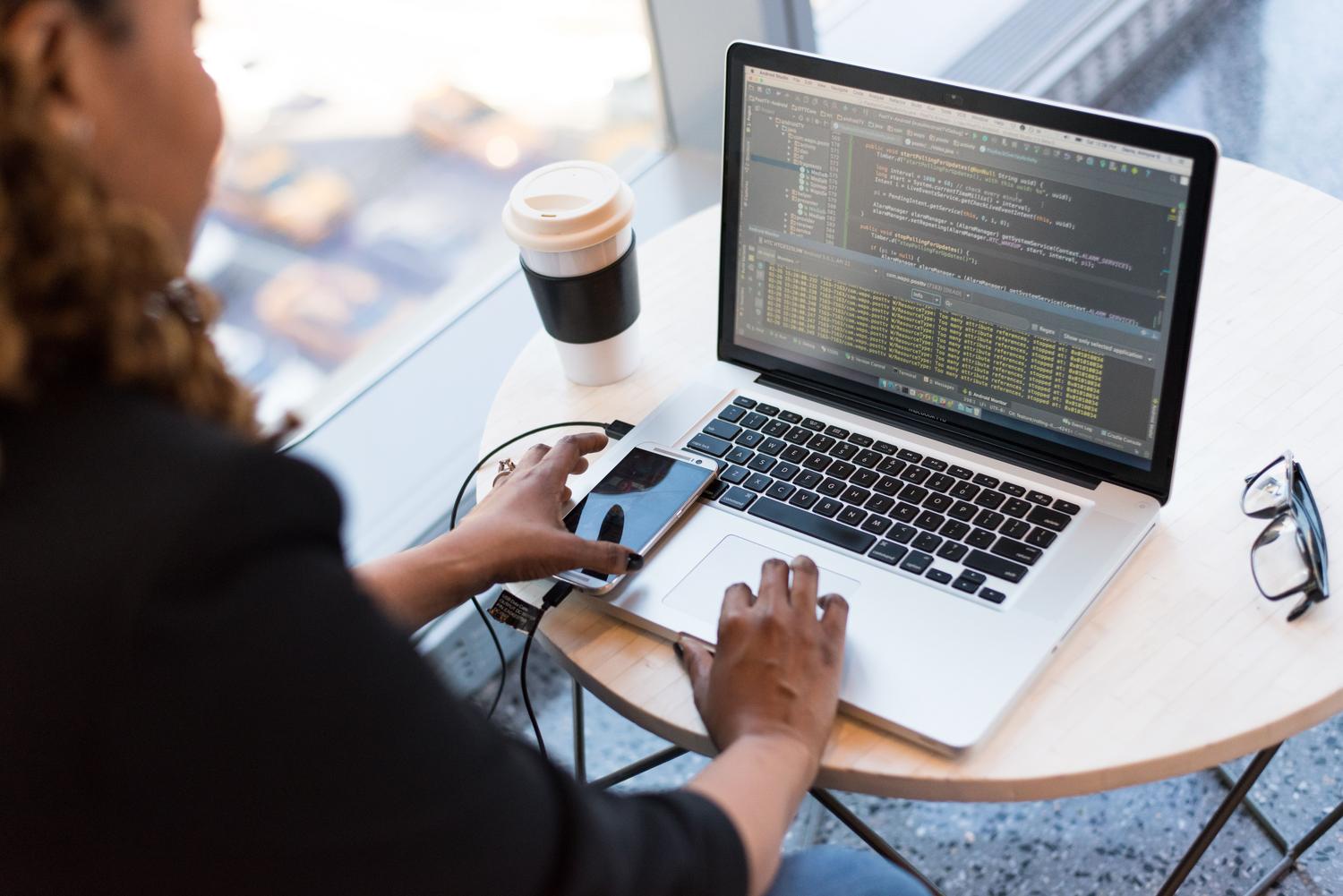 Desarrolladora integrando SDKs de Firebase en app móvil Desarrolladora trabajando en una aplicación móvil conectada a su laptop, ilustrando la integración de SDKs de Firebase.