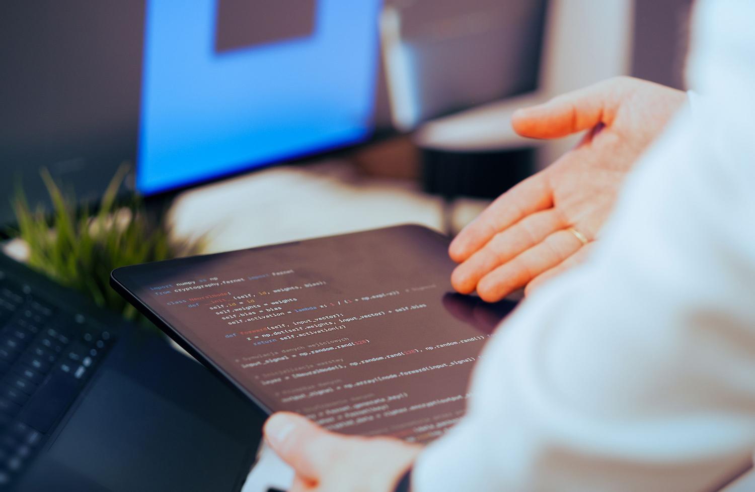 Desarrollador de software analizando código de redes neuronales en una tablet, representando la implementación técnica de la IA mediante Azure AI y PaaS.