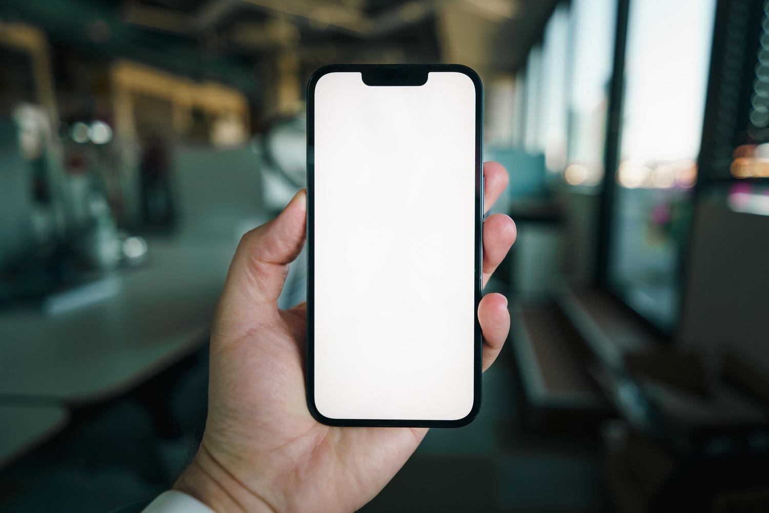 Primer plano de una mano sosteniendo un smartphone con pantalla en blanco en una oficina, ideal para tutoriales