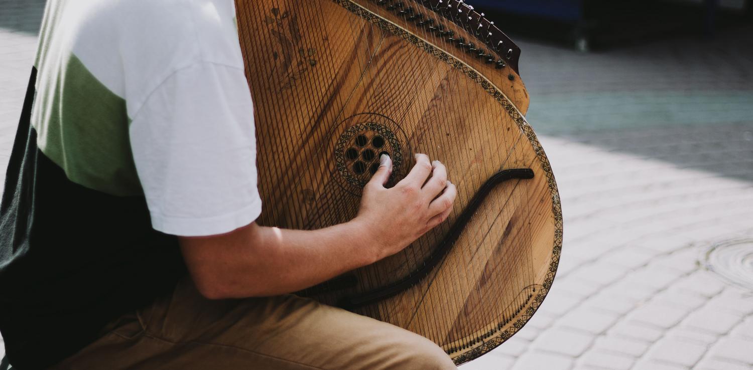 Músico tocando un instrumento de cuerda tradicional al aire libre, representando el rol del bardo Jaskier