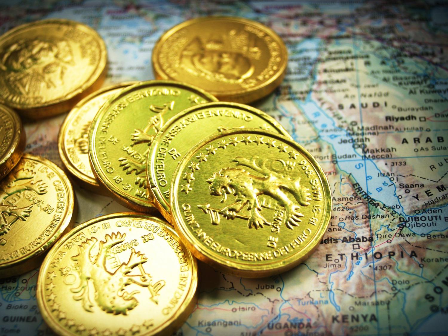 Monedas de oro sobre un mapa antiguo, simbolizando las recompensas y el farmeo de recursos en los juegos de rol.