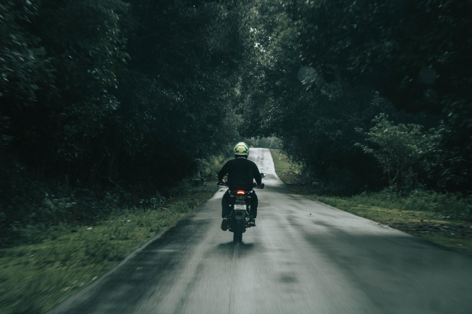 Un motorista solitario conduciendo por una carretera serena bordeada de árboles, representando la paz mental y el reset emocional.