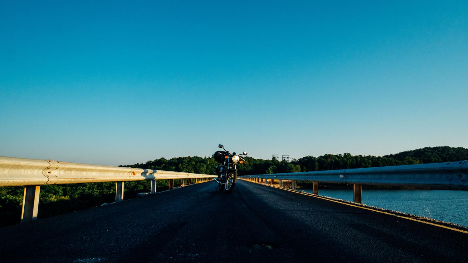 Motocicleta estacionada en un puente al atardecer bajo un cielo despejado, simbolizando la libertad y el bienestar emocional.