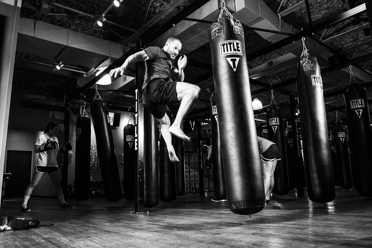 Luchador de artes marciales ejecutando una patada potente en un gimnasio, ilustrando la fuerza bruta y el impacto del Estilo Brusco de Urshifu.