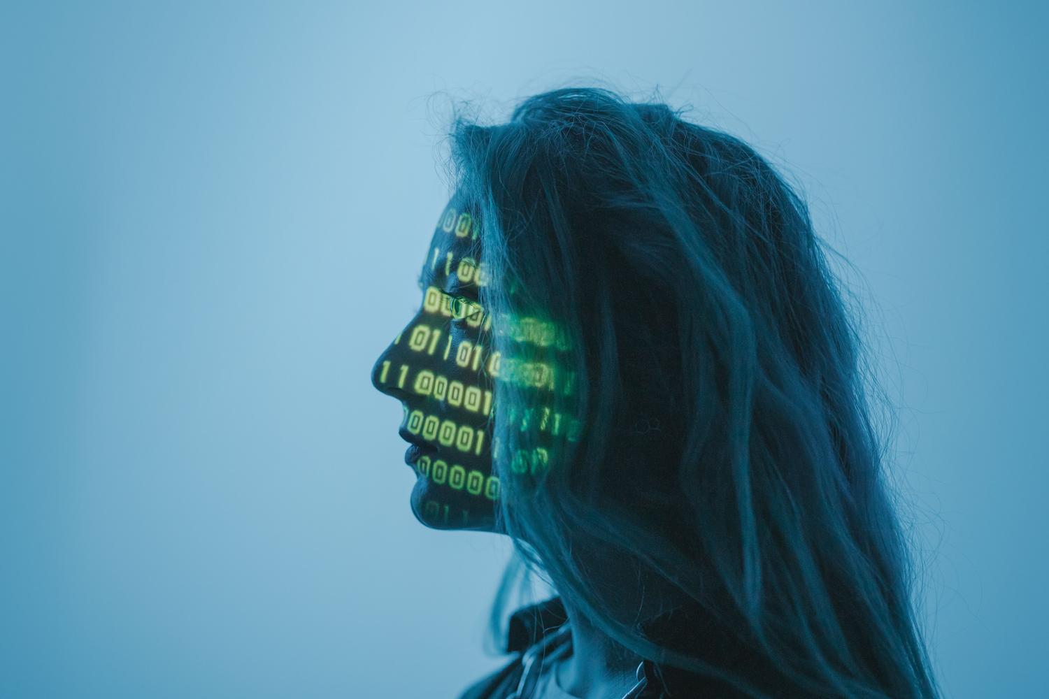 Retrato conceptual de una persona con código binario proyectado sobre su rostro, representando la naturaleza digital de la identidad y los activos de intimidad.