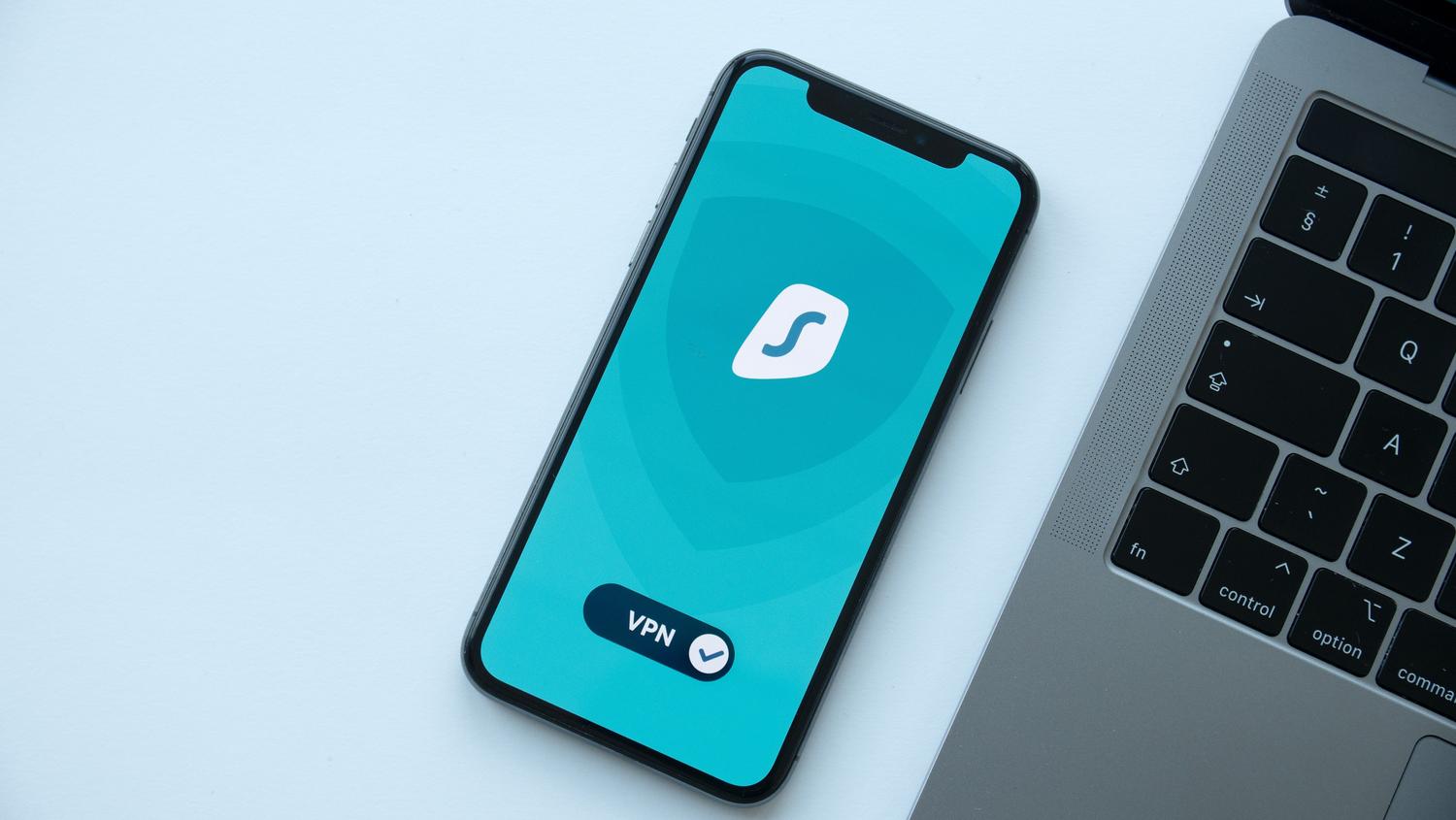 Vista cenital de un smartphone con una VPN activa junto a un ordenador portátil en un escritorio profesional.