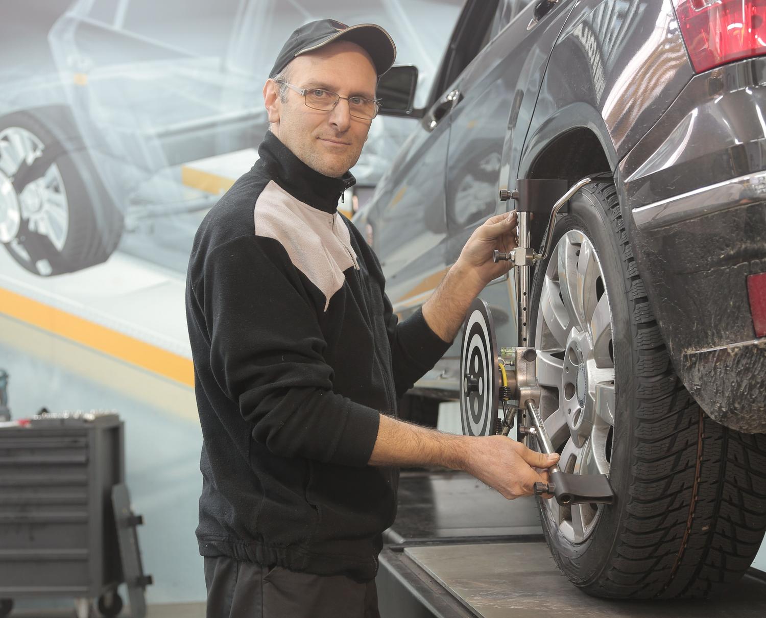 Mecánico profesional realizando el equilibrado y alineación de las ruedas de un coche en un taller especializado.
