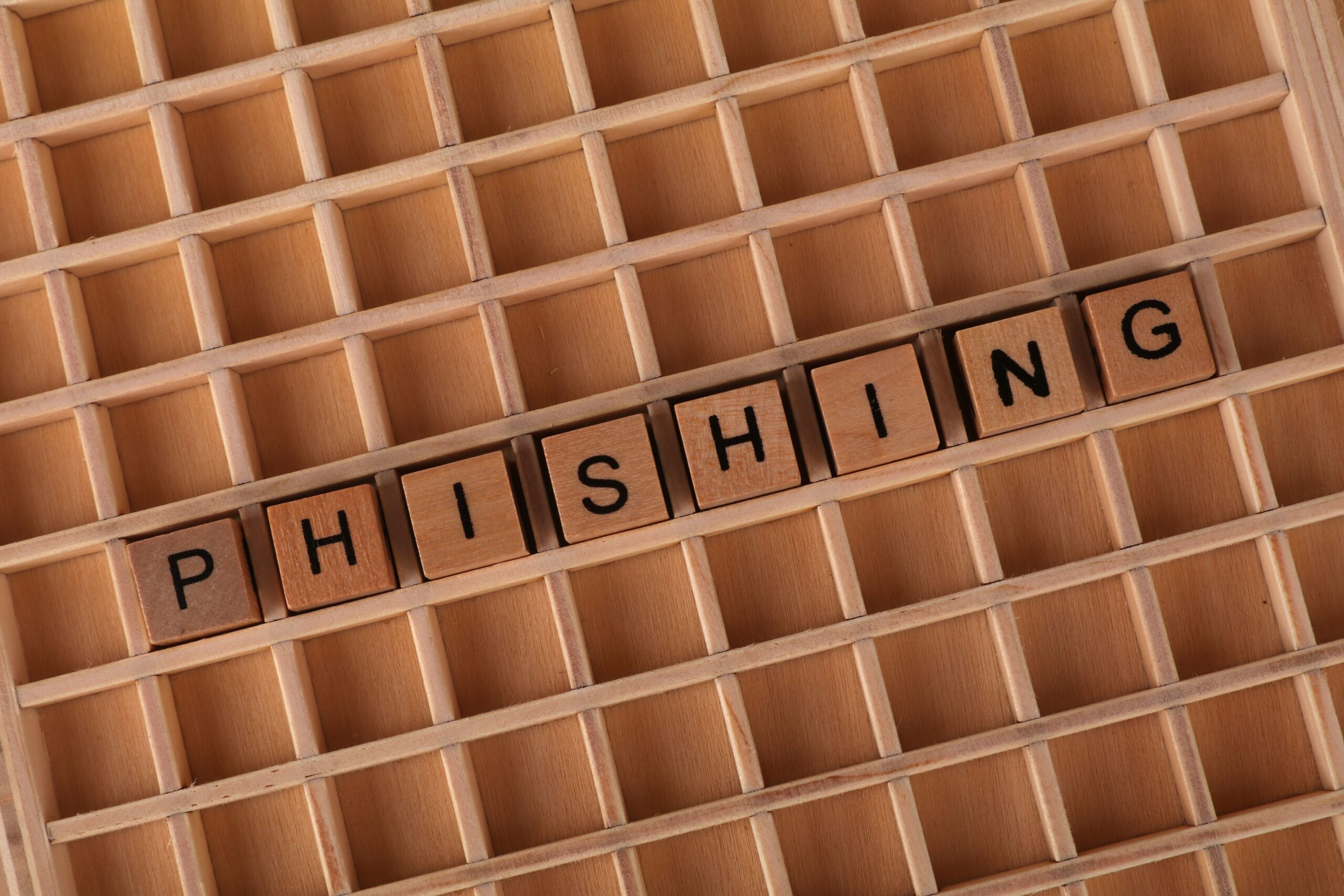 Letras de madera formando la palabra PHISHING sobre una cuadrícula, representación conceptual de la estafa.