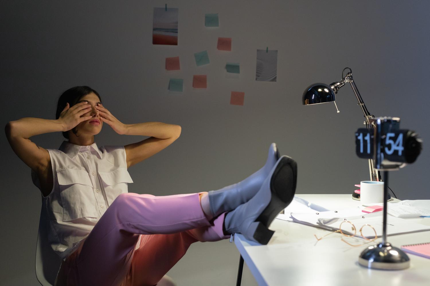 Mujer recostada en su silla de oficina cubriendo sus ojos con las manos para descansar la vista tarde por la noche.