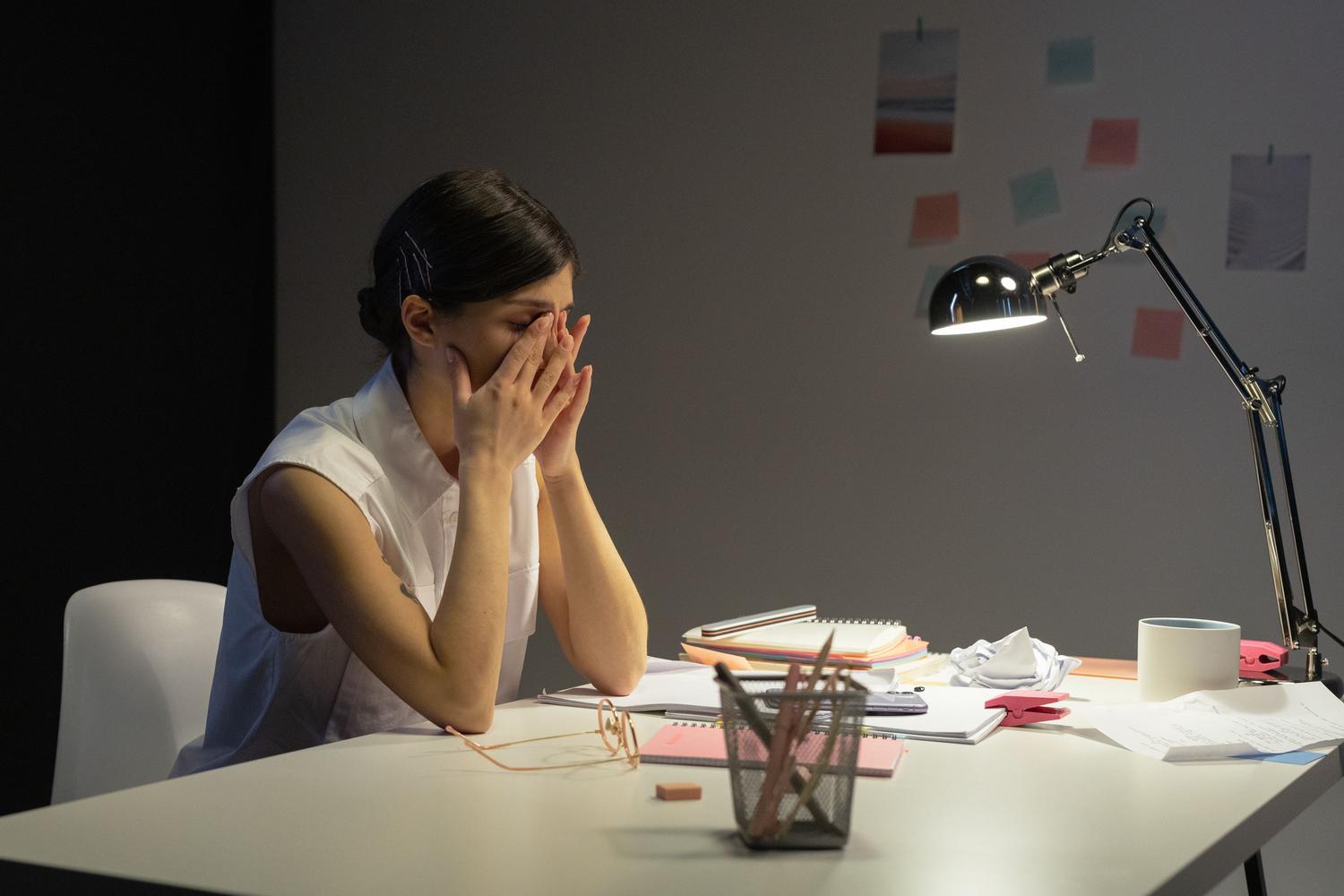 Mujer profesional agotada frotándose los ojos durante una jornada laboral nocturna frente a su escritorio.