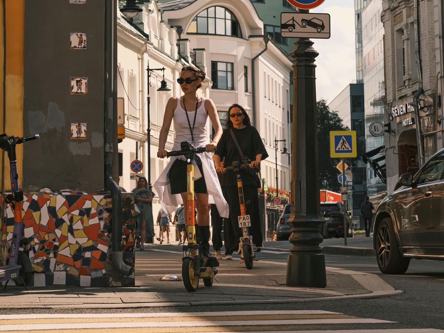 Dos mujeres desplazándose por la ciudad en scooters eléctricos, transmitiendo una experiencia de transporte urbana eficiente y placentera.