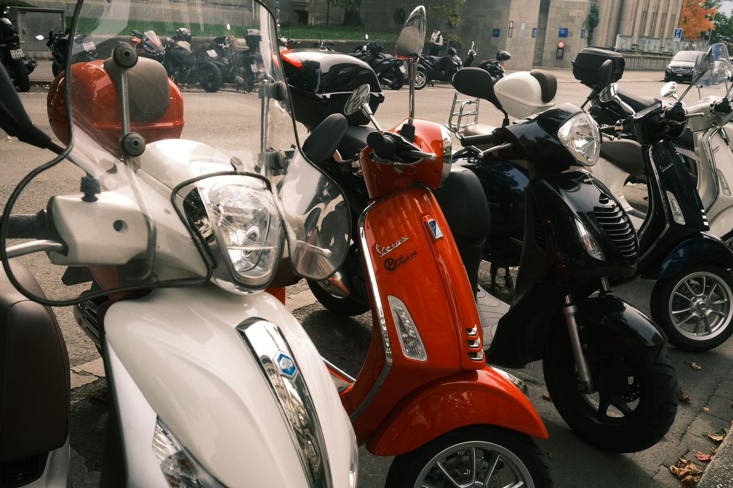 Fila de scooters modernos aparcados en una calle urbana, resaltando la agilidad y facilidad de estacionamiento en la ciudad.