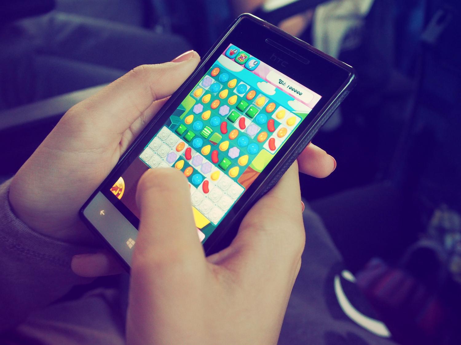 Primer plano de unas manos sosteniendo un smartphone con un juego de puzles colorido en pantalla, representando la variedad de títulos disponibles.