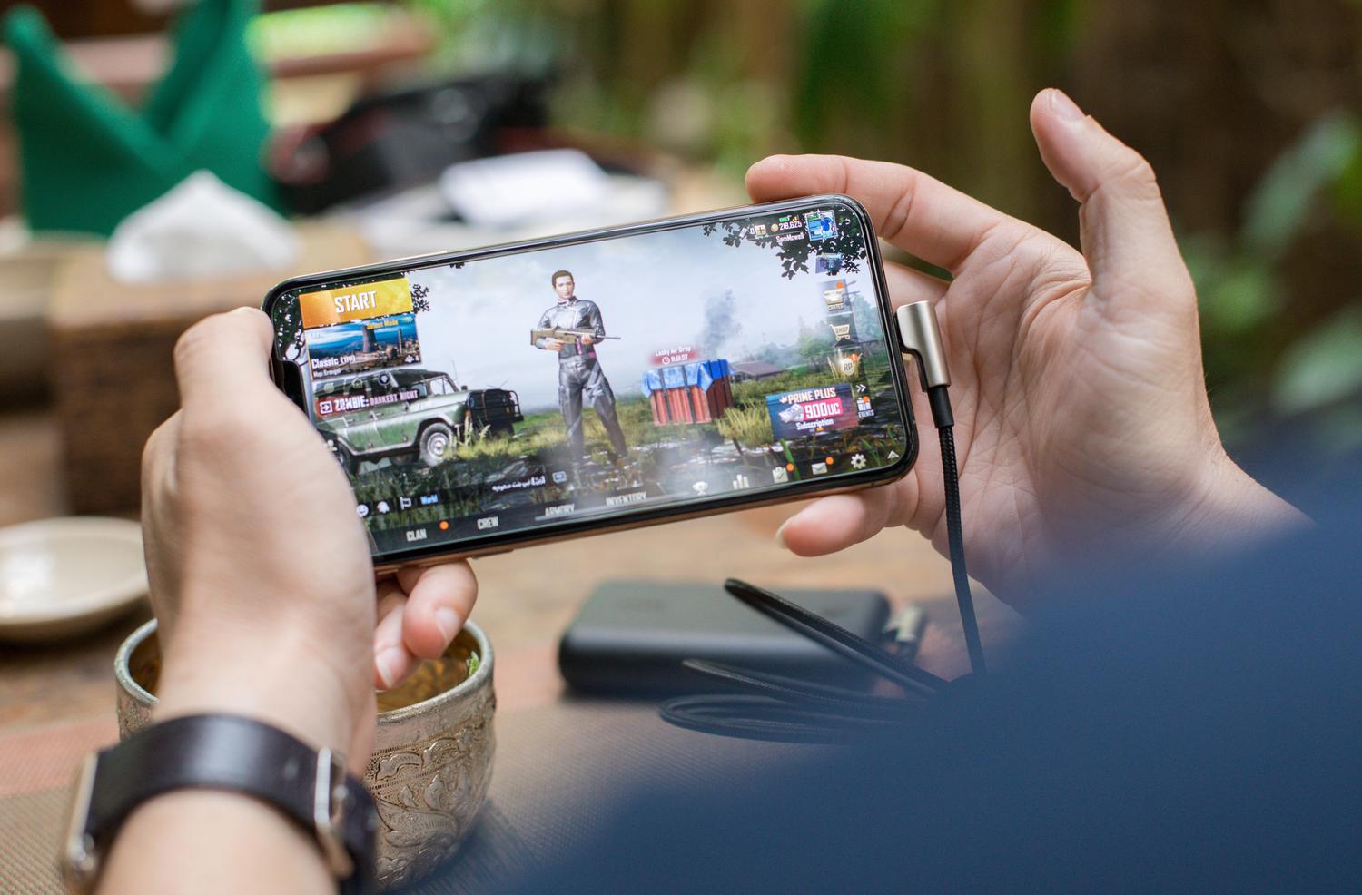 Persona utilizando un smartphone para jugar al aire libre, destacando la portabilidad y la posibilidad de retomar partidas en cualquier lugar.
