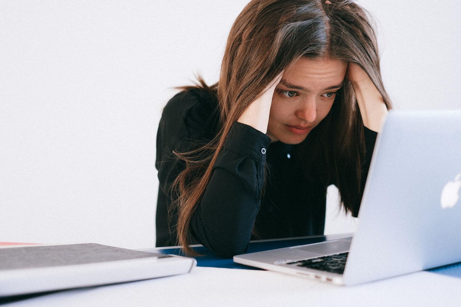 Mujer estresada con las manos en la cabeza mirando la pantalla de su laptop, reflejando la frustración por errores técnicos persistentes en el software.