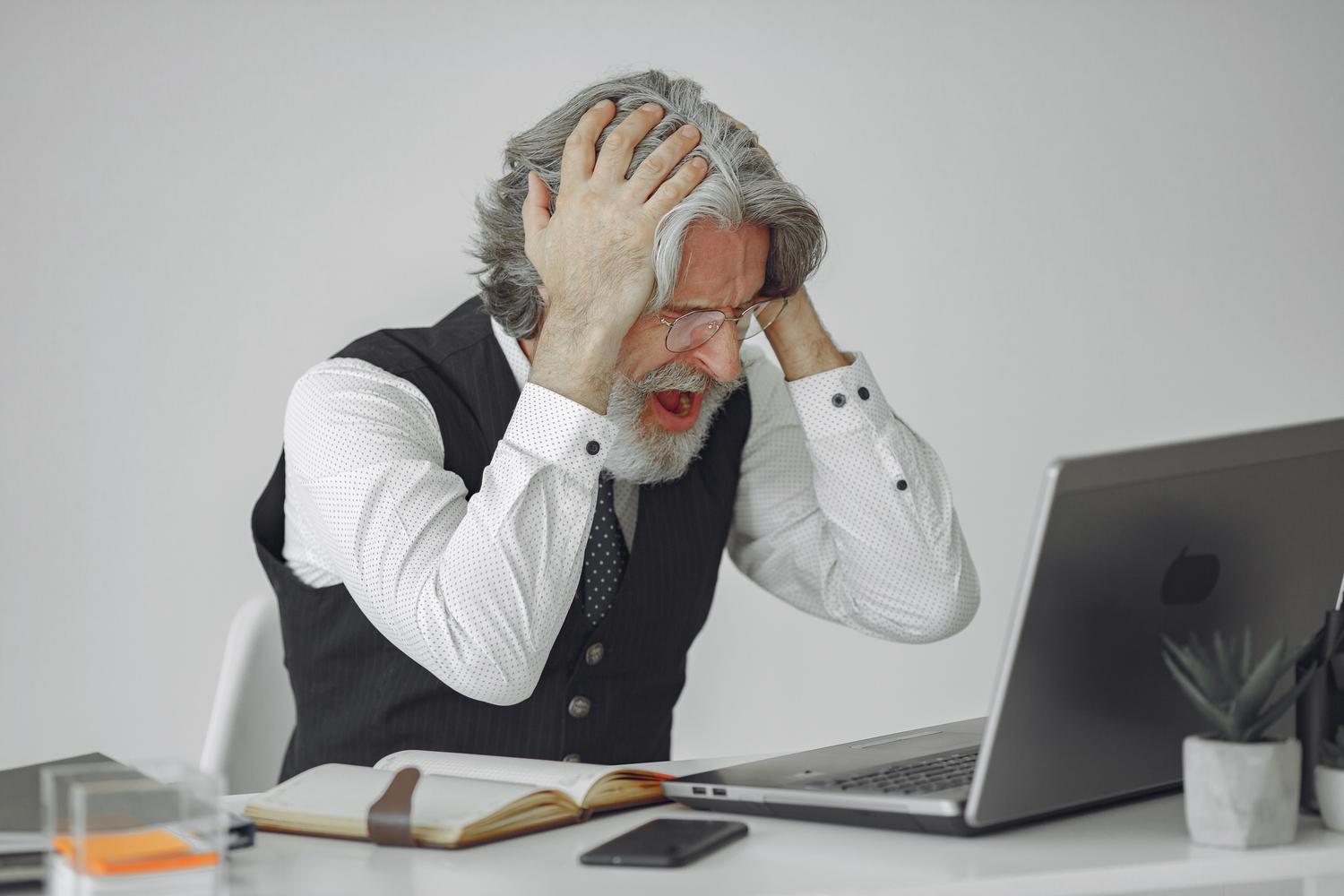 Hombre frustrado gritando frente a su computadora en una oficina, representando la desesperación al encontrar un error de inserción de celdas en Excel.