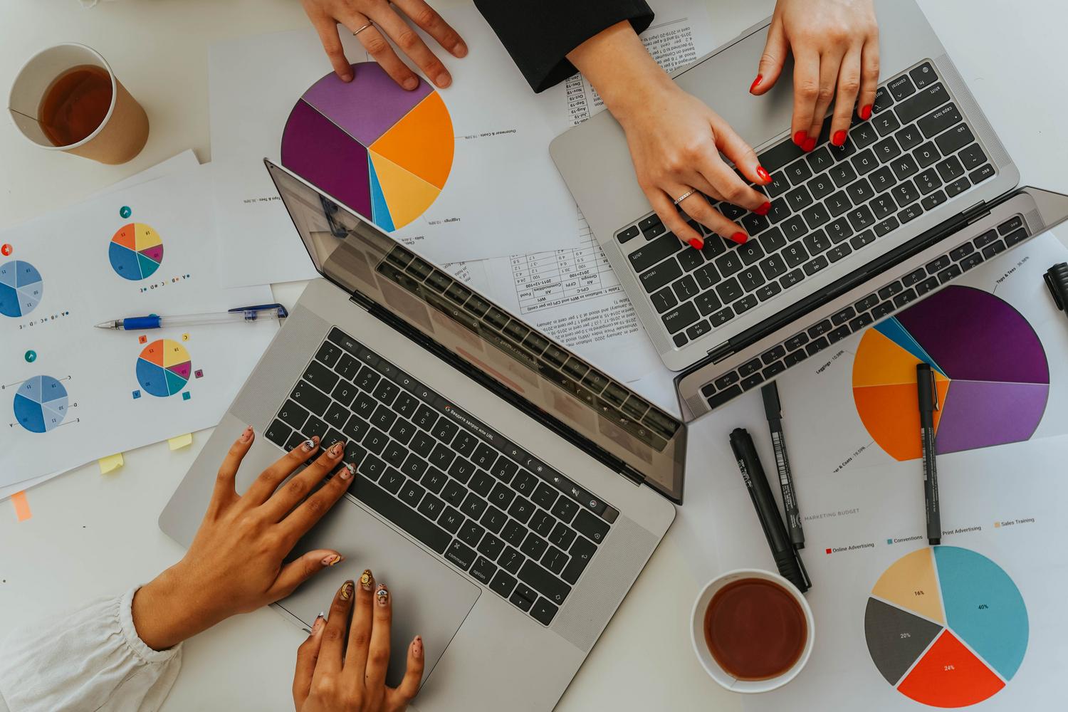 Vista cenital de equipo de trabajo analizando gráficos y datos en laptops, ilustrando el contexto profesional de uso de hojas de cálculo.