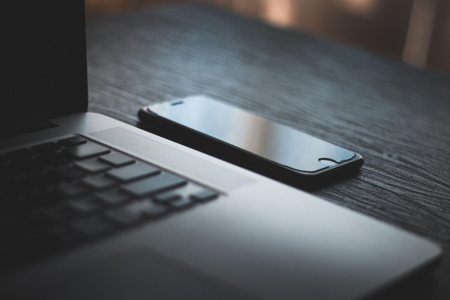 Un ordenador portátil y un teléfono inteligente sobre un escritorio de madera, representando la sincronización de WhatsApp Web.