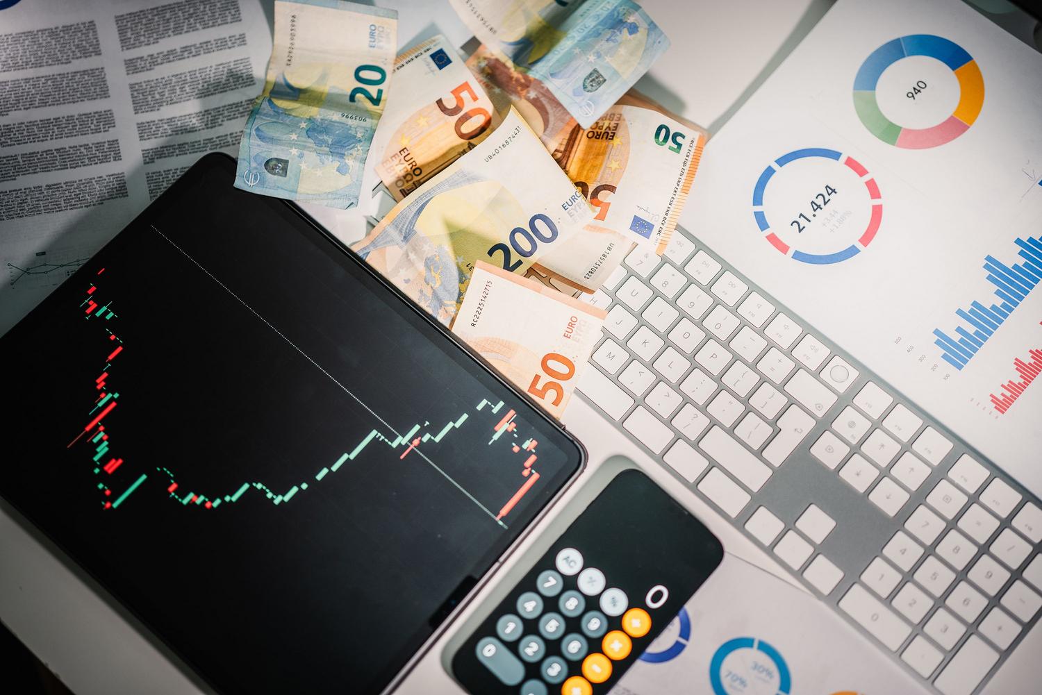 Vista cenital de herramientas financieras, tablet con gráficos de mercado y billetes de euro, ideal para ilustrar el análisis de rentabilidad.