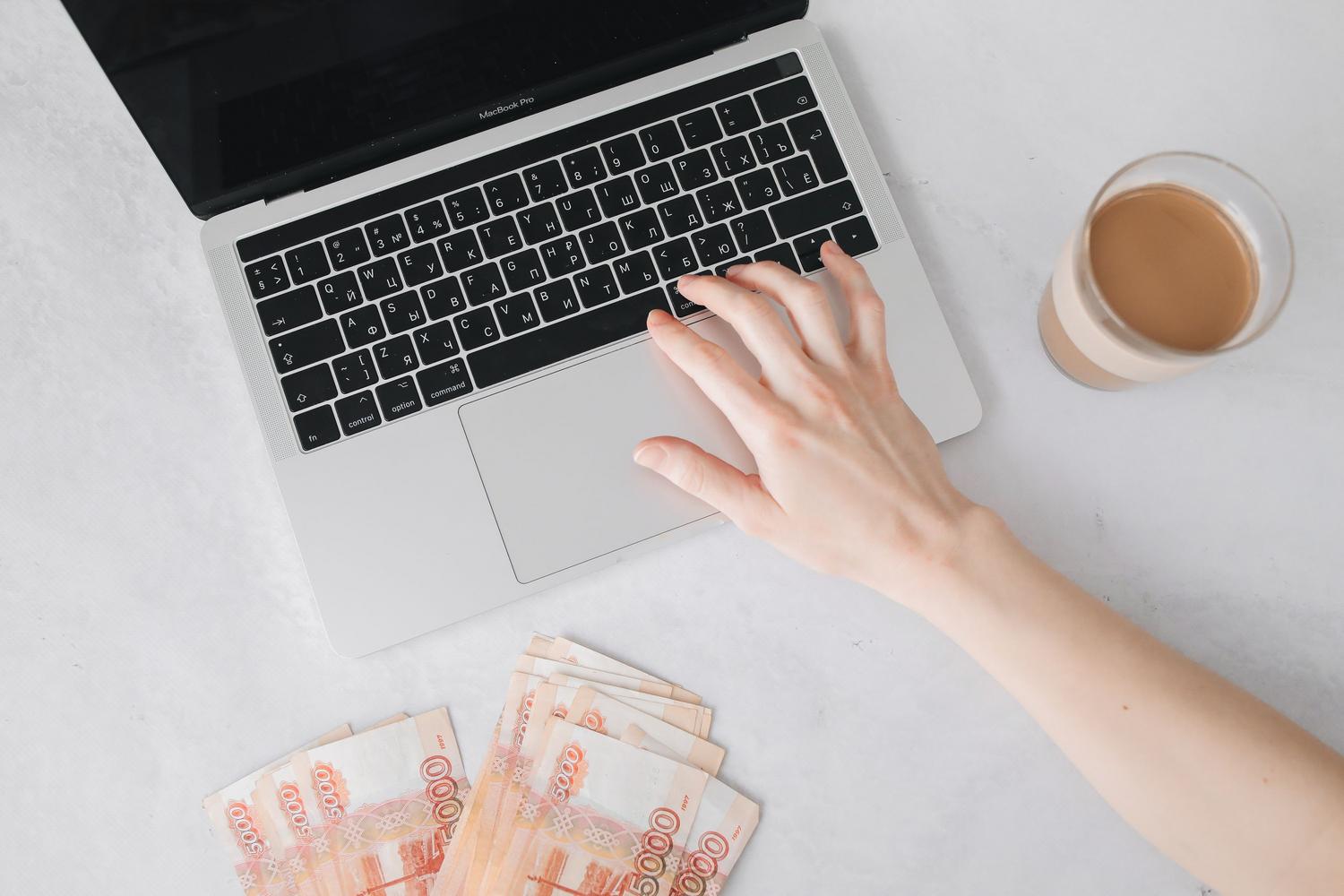 Primer plano de una persona trabajando en un portátil con dinero y café sobre la mesa, representando el estilo de vida del emprendedor digital.