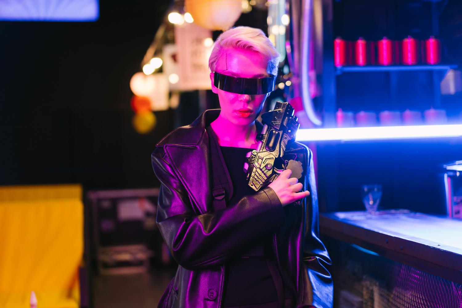 Mujer con estética cyberpunk y visor tecnológico sosteniendo un arma avanzada en un entorno de luces neón.