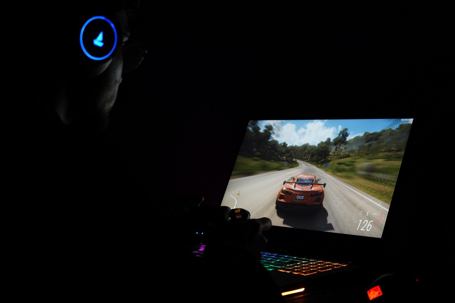 Gamer utilizando un ordenador portátil potente con auriculares en un entorno oscuro con luces ambientales, ilustrando el mundo gaming.