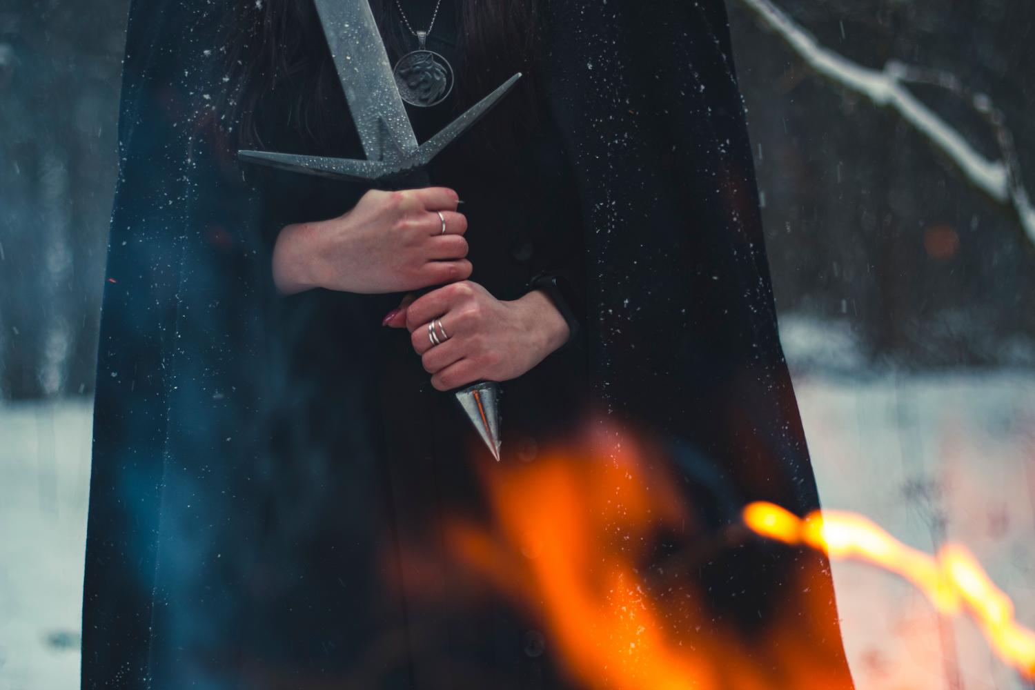 Figura misteriosa con espada entre nieve y llamas, evocando la atmósfera oscura y el desafío del endgame de Path of Exile 2.