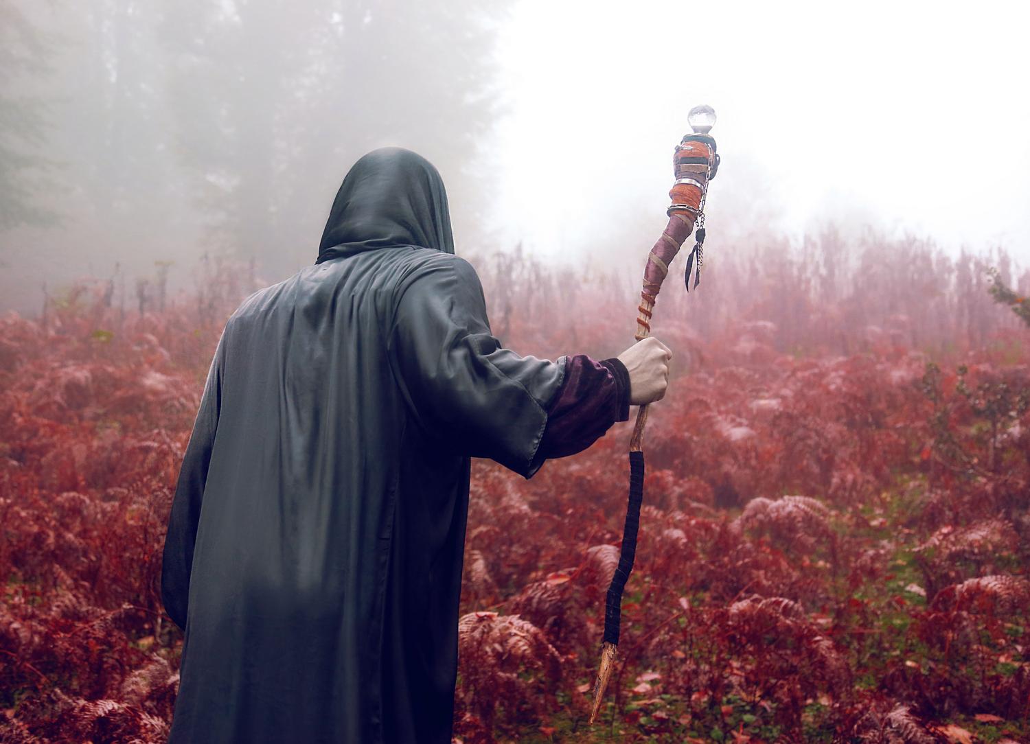 Figura encapuchada con un bastón mágico en un bosque brumoso, representando las builds de lanzadores de hechizos (Spellcasters).