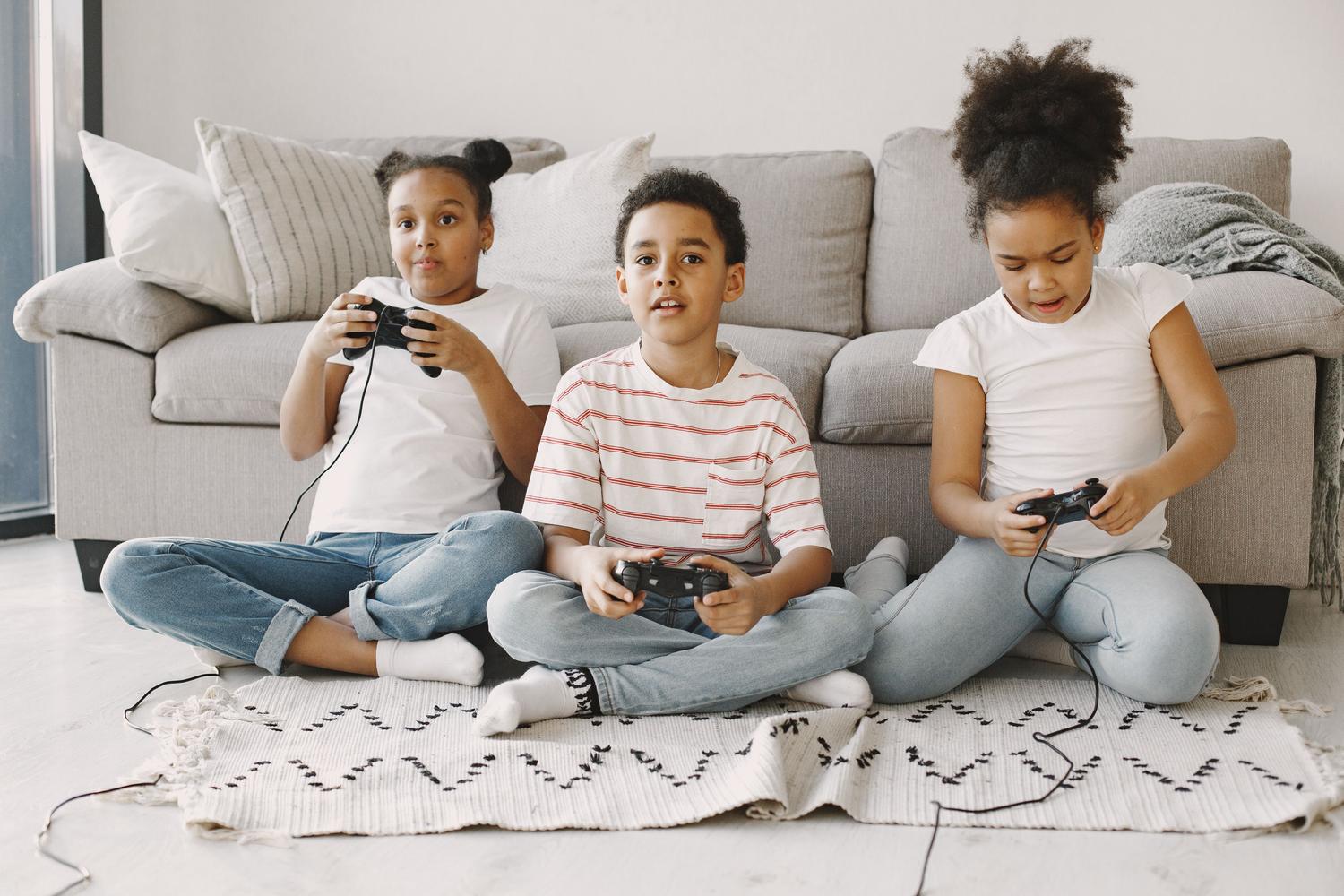 Grupo de tres niños jugando videojuegos en el suelo de su casa, resaltando el aspecto social de la versión Junior.