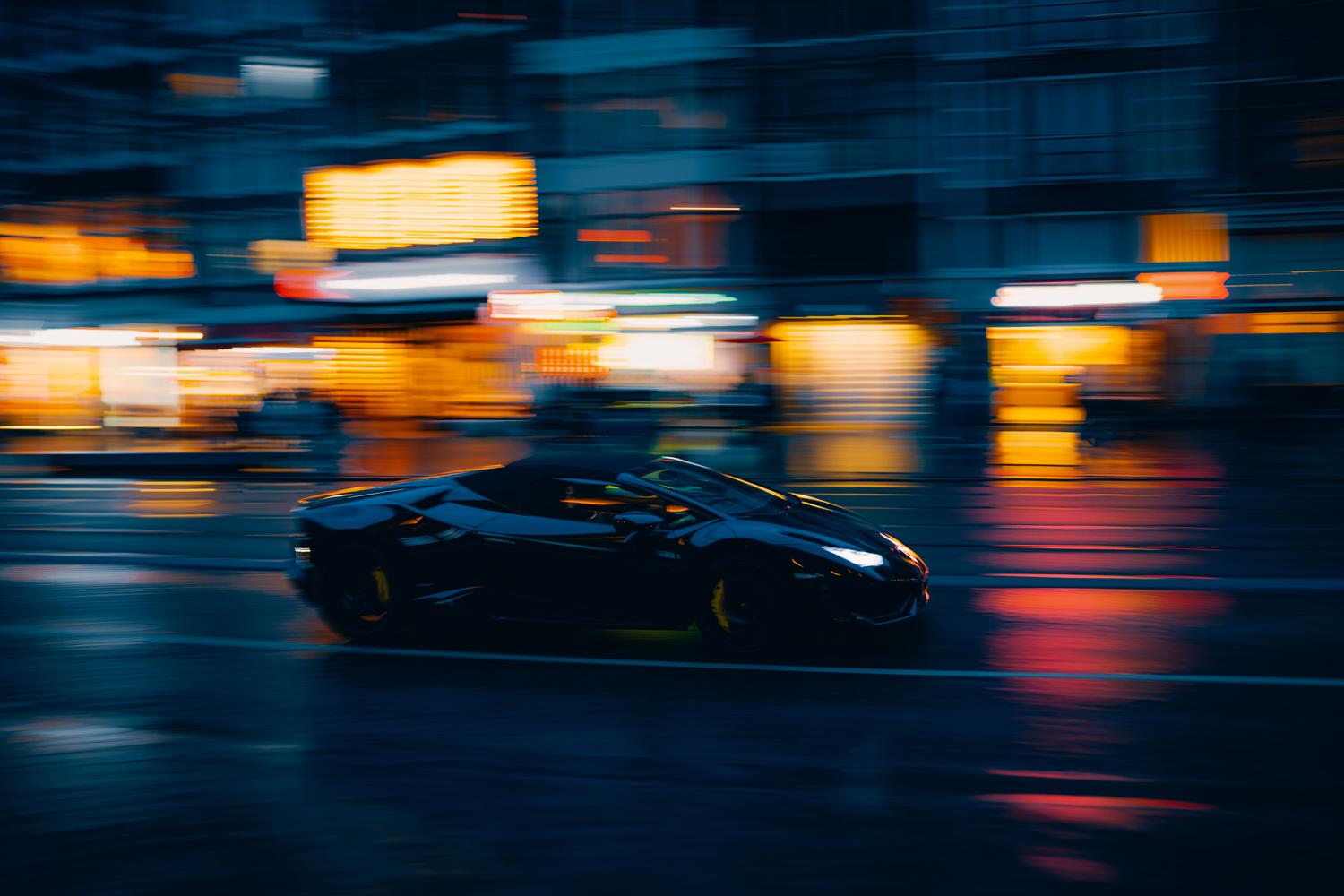 Coche deportivo negro circulando a alta velocidad por una ciudad iluminada de noche.