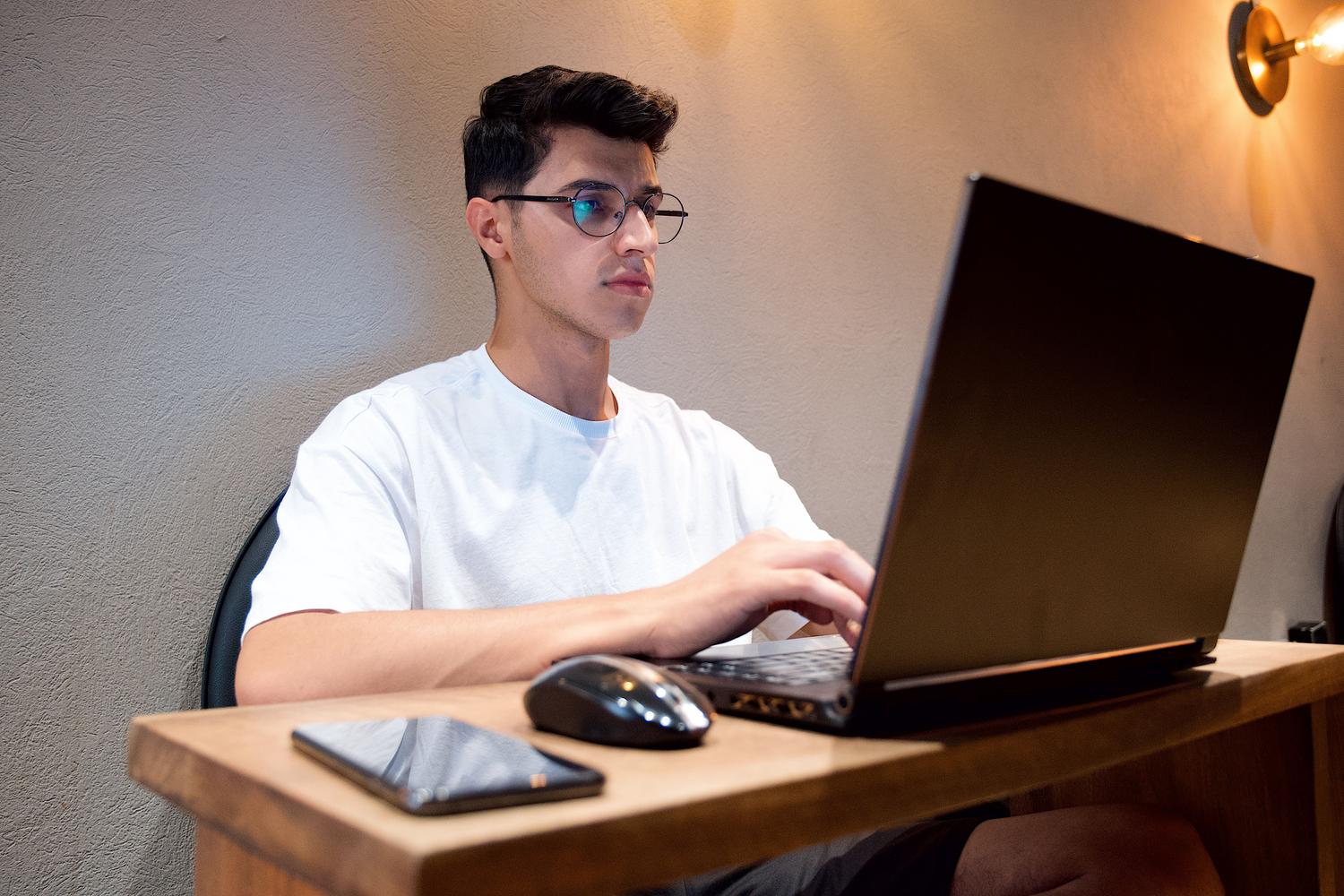 Hombre trabajando en un escritorio con ordenador portátil y teléfono móvil, mostrando un entorno de trabajo digital organizado.