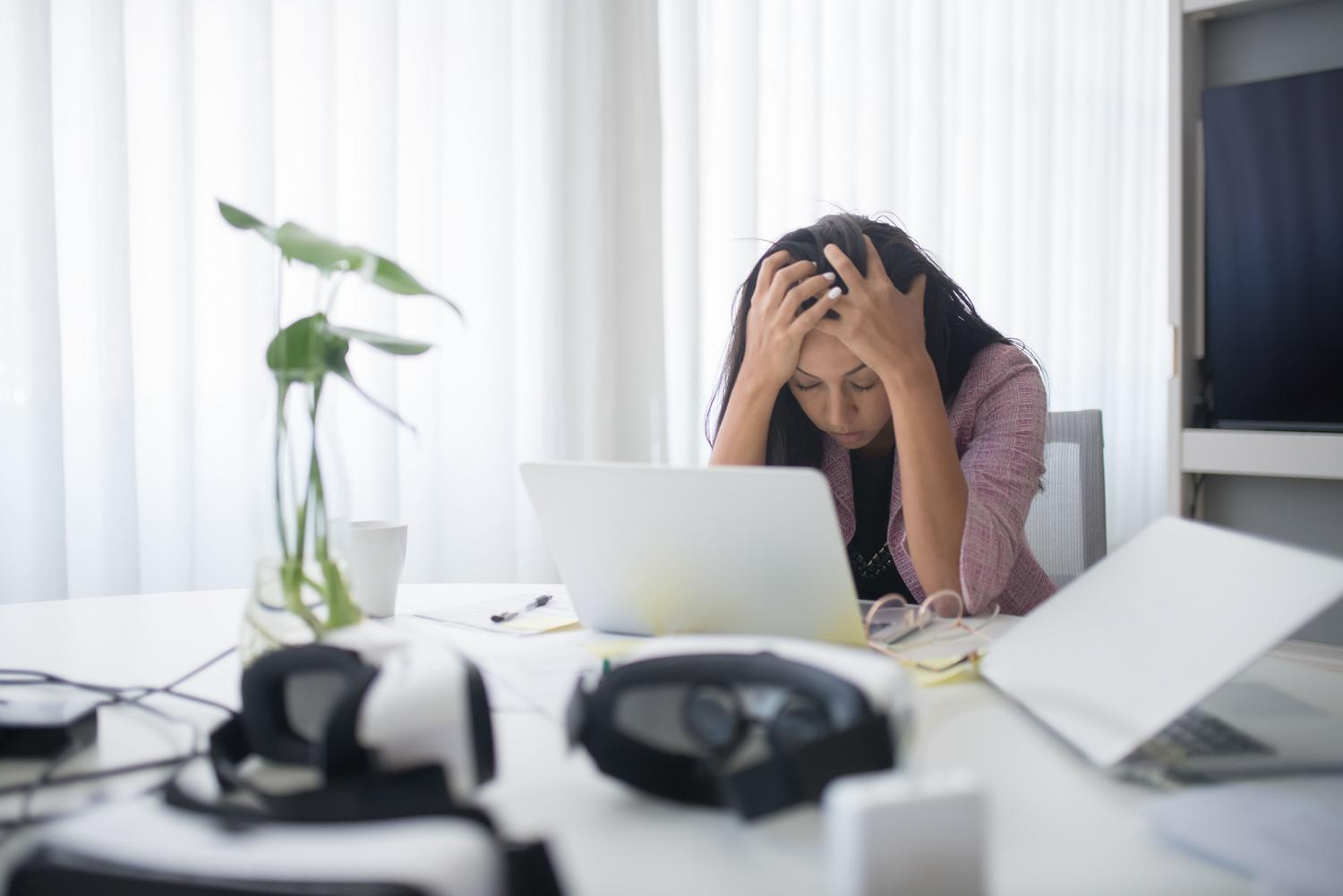 Mujer estresada trabajando con un ordenador portátil en una oficina moderna, representando la frustración por las notificaciones intrusivas.