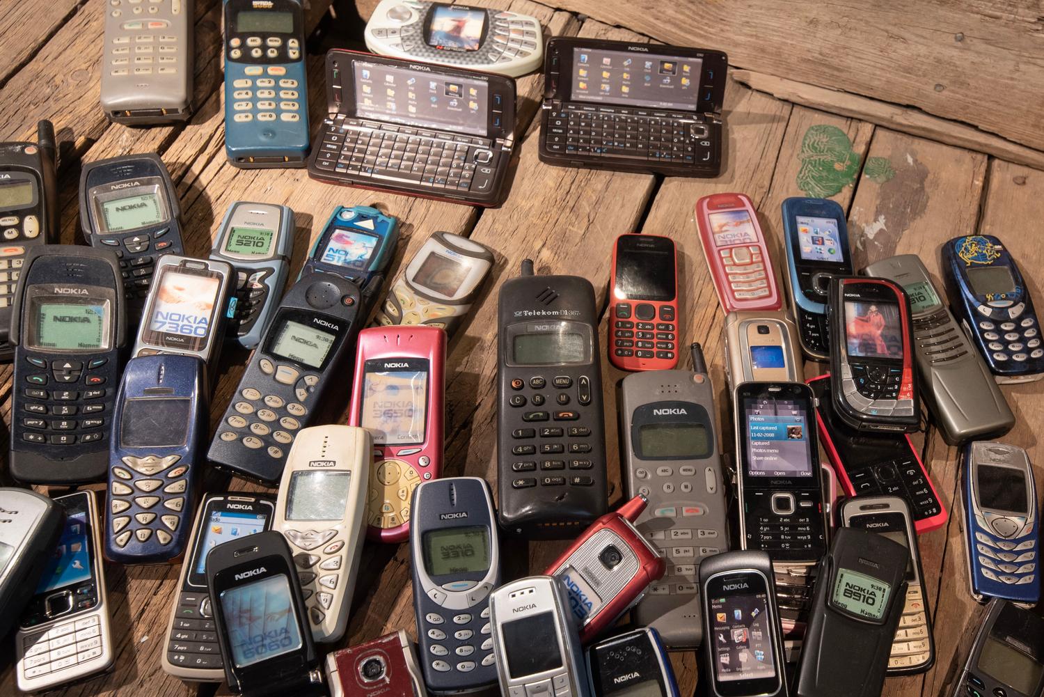 Colección de teléfonos móviles antiguos y obsoletos sobre una superficie de madera, simbolizando el fin de las tecnologías 2G y 3G.