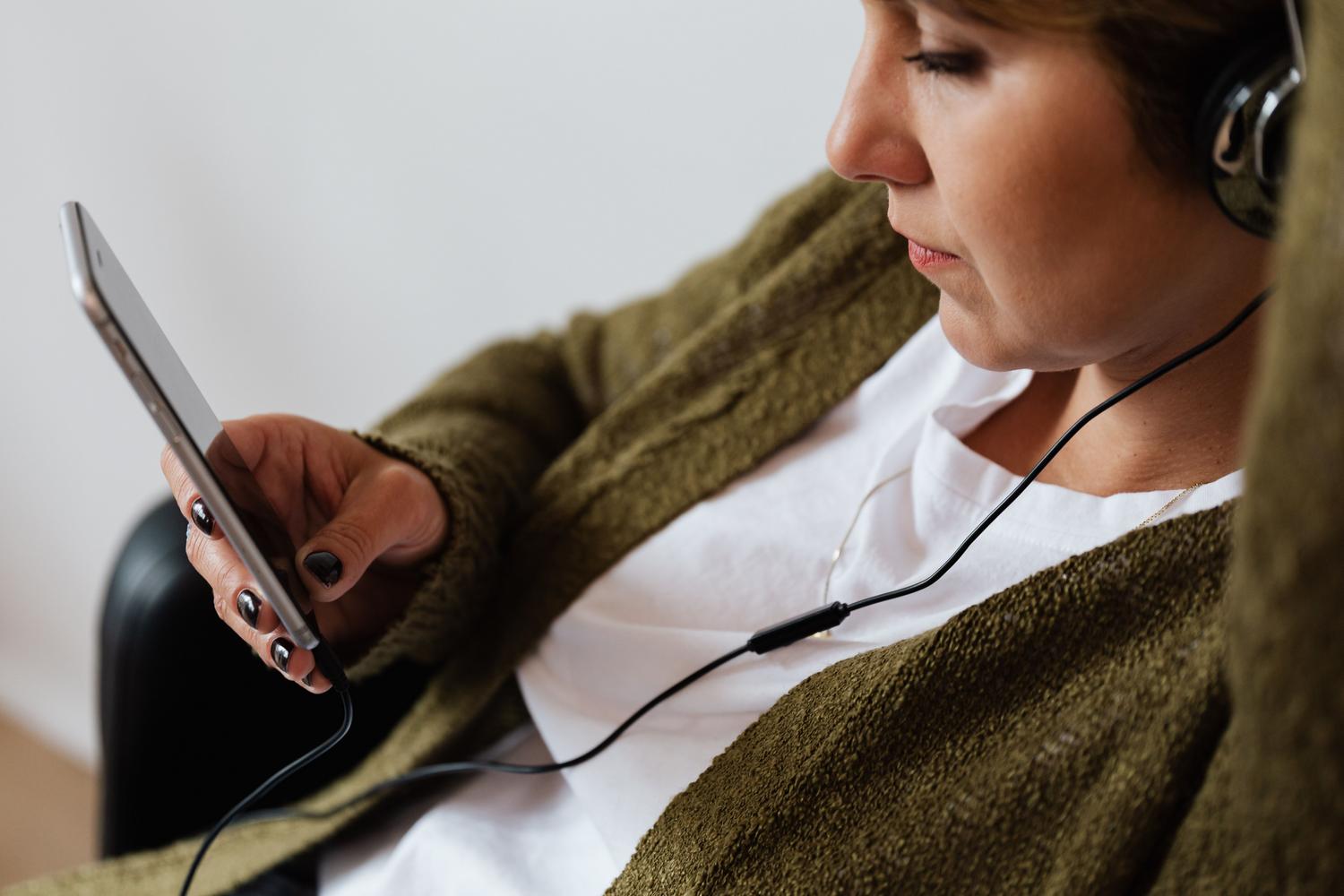 Mujer escuchando música con auriculares de diadema y un smartphone, representando el disfrute de contenido multimedia.