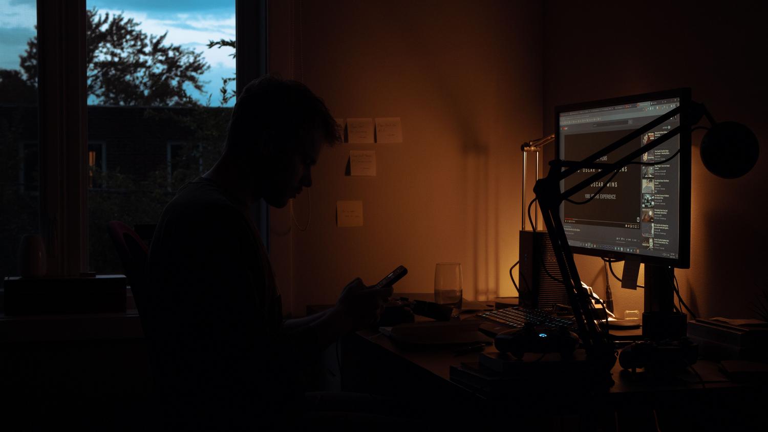 Silueta de un usuario en la penumbra iluminado por su pantalla, representando los riesgos digitales invisibles y el anonimato.