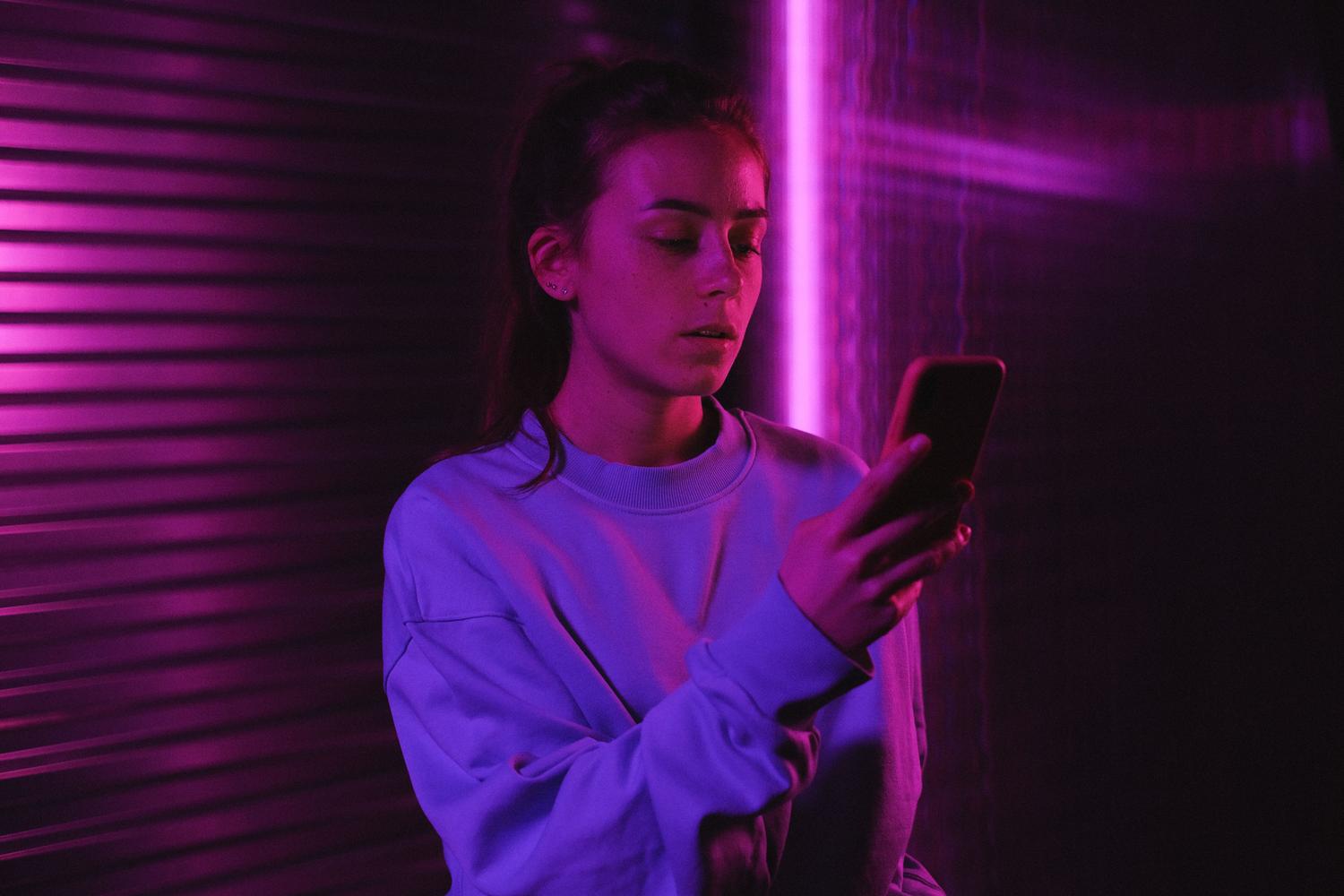 Joven de la Generación Z utilizando su smartphone bajo luces neón, reflejando la simbiosis constante y la cultura visual de esta generación.