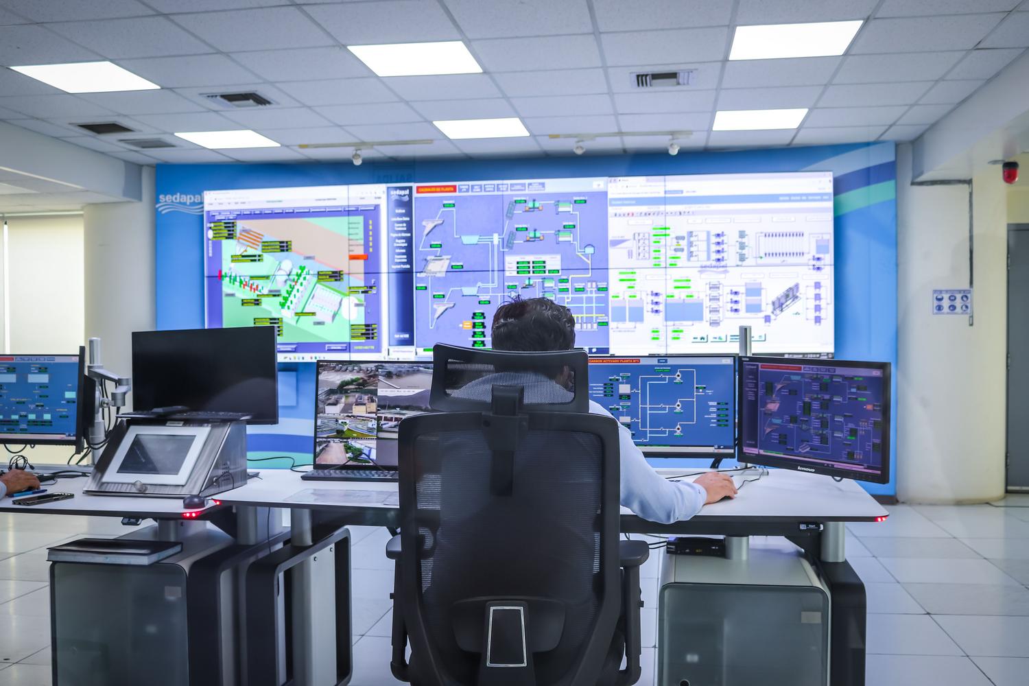 Operador supervisando sistemas de control industrial SCADA en una sala de mando moderna.