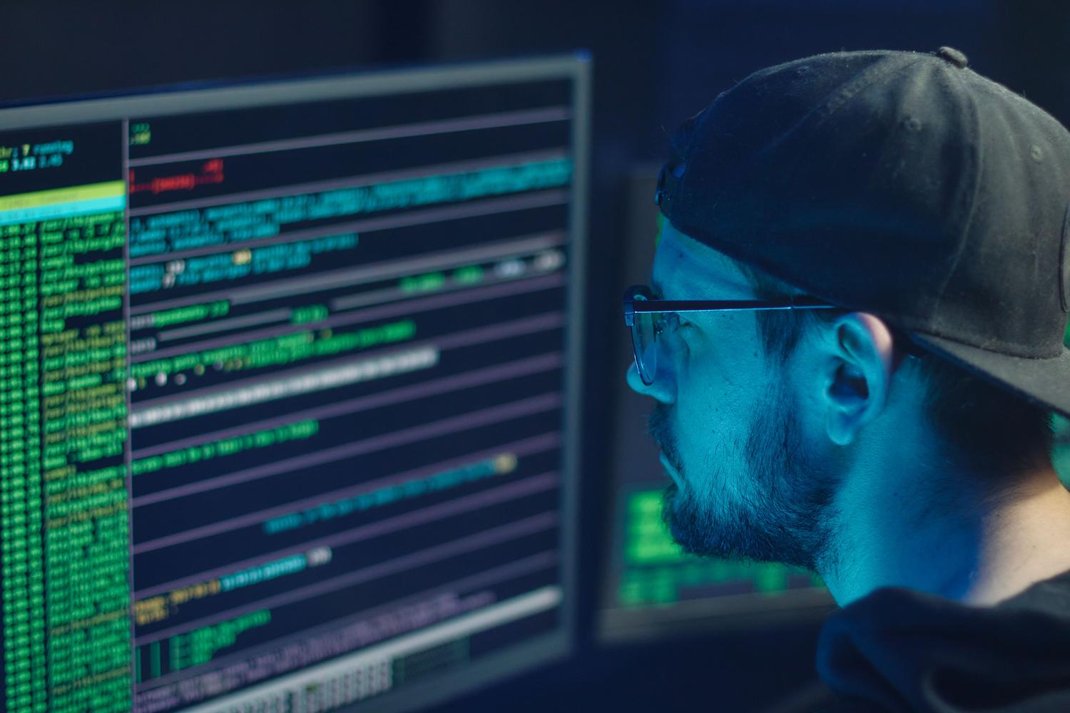 Experto en ciberseguridad supervisando líneas de código en múltiples monitores para detectar anomalías en la red.