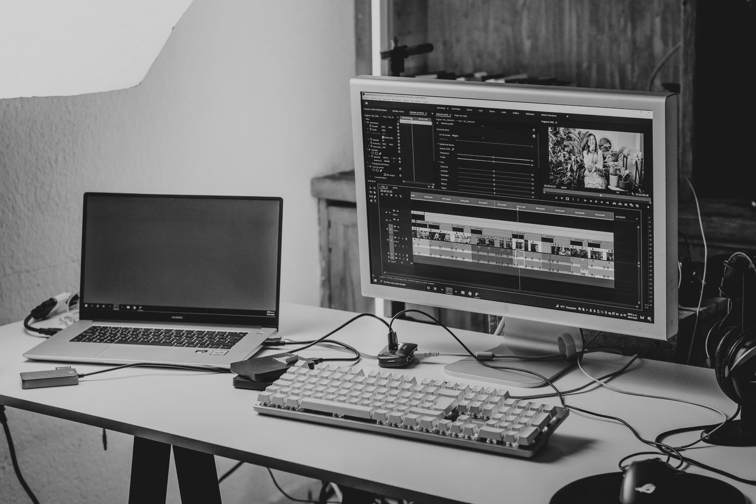 Espacio de trabajo profesional con monitor y portátil configurado para la edición de vídeo y gestión de archivos.