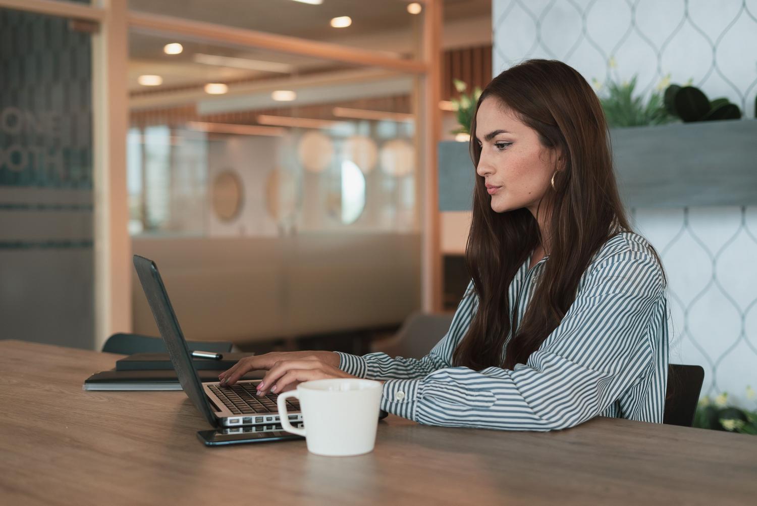Mujer profesional trabajando en una oficina moderna con su laptop, ilustrando la productividad y eficiencia laboral gracias a la IA.