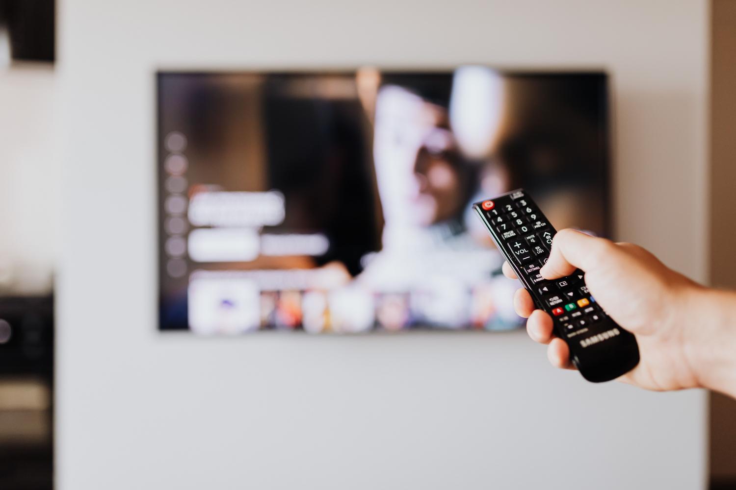 Persona utilizando el mando a distancia de una televisión, enfocando la acción de navegar por la interfaz para buscar aplicaciones y comprobar la compatibilidad.